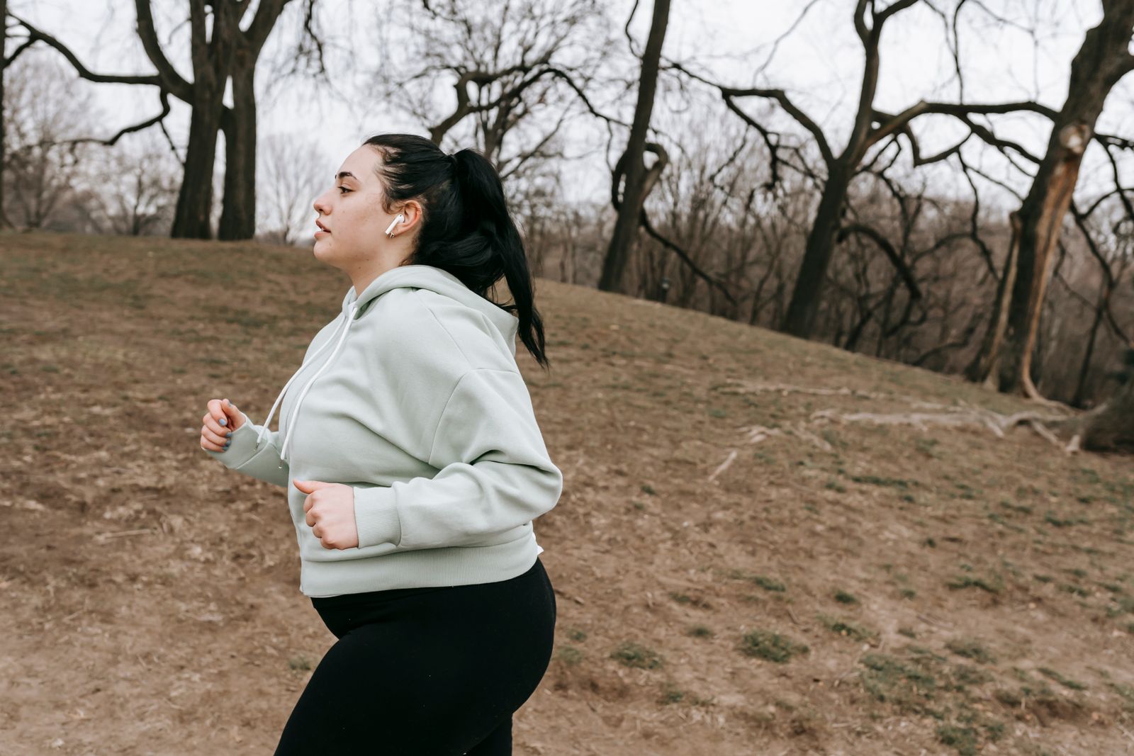 Woman jogging beside a tree-lined park path.