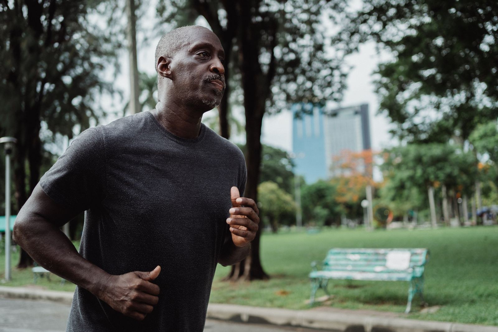 A man jogging on a park path beneath trees.
