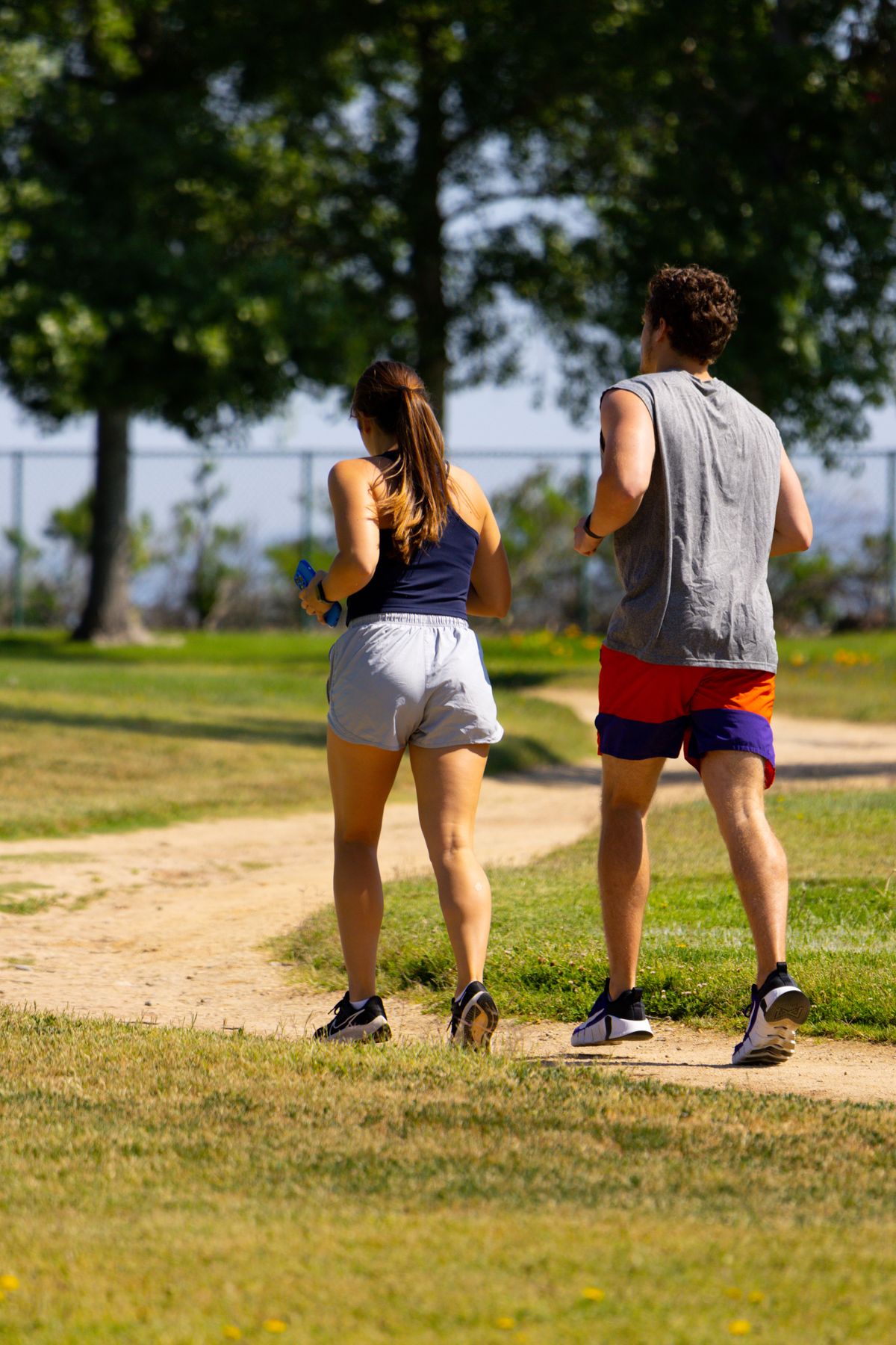 Two runners moving side by side along a sunny park path.
