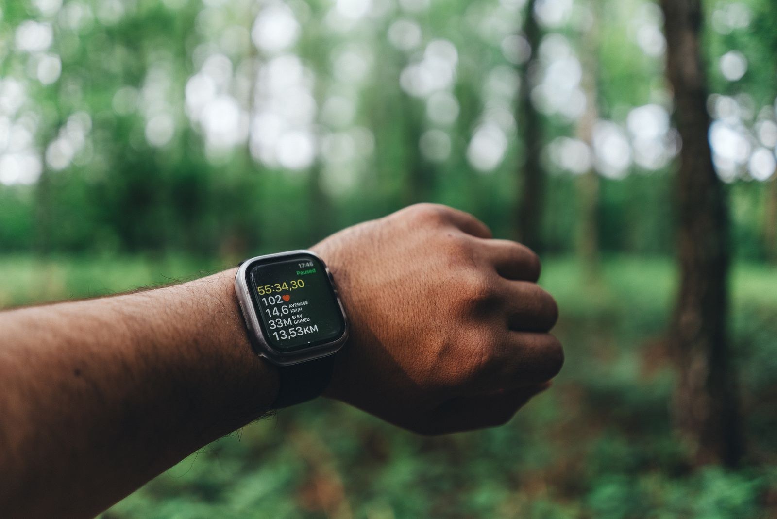 A running watch showing workout metrics in front of woodland.