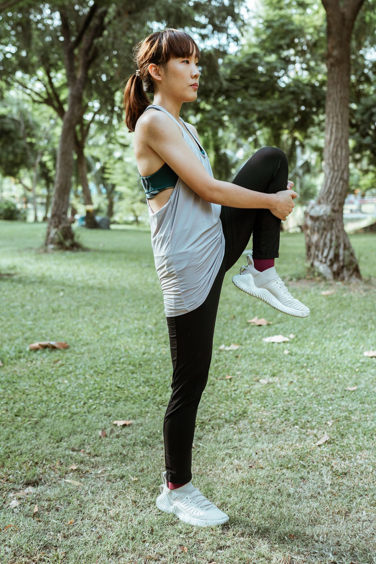 A woman raises one knee while warming up in a park.