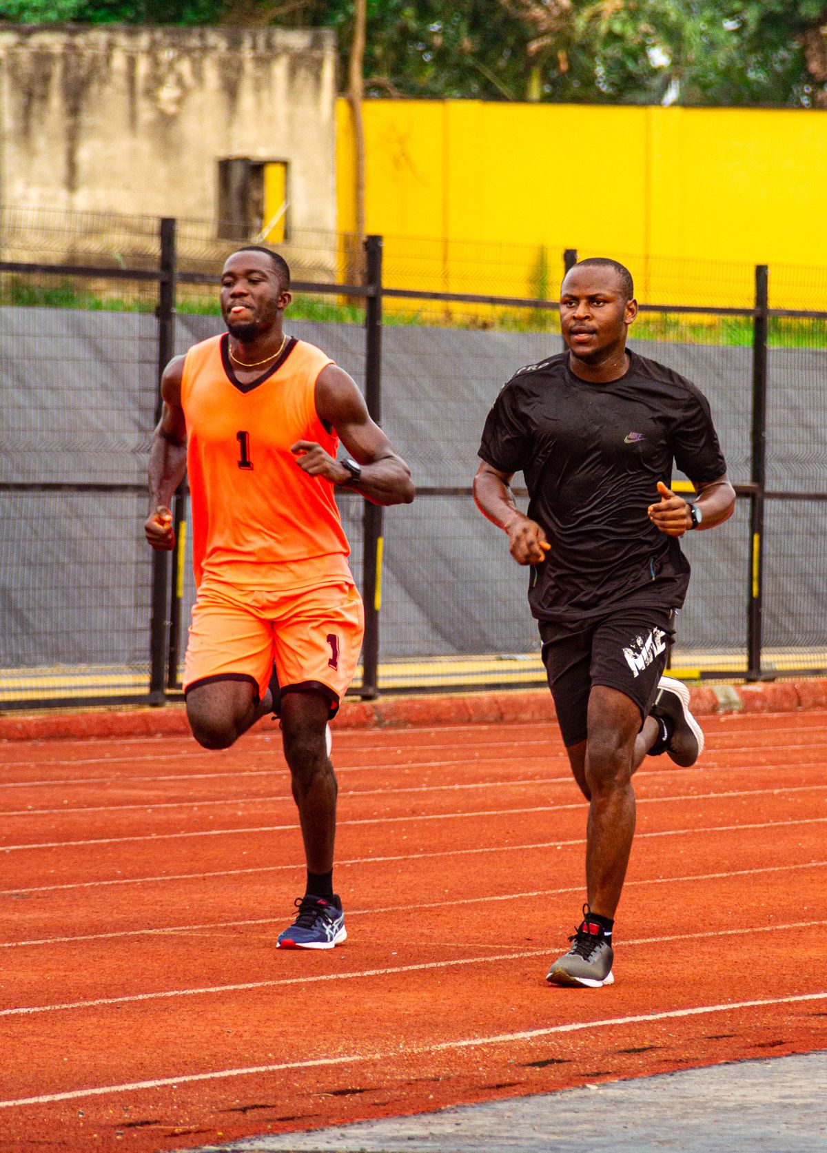 Two runners accelerate along separate lanes of a clear athletics track.