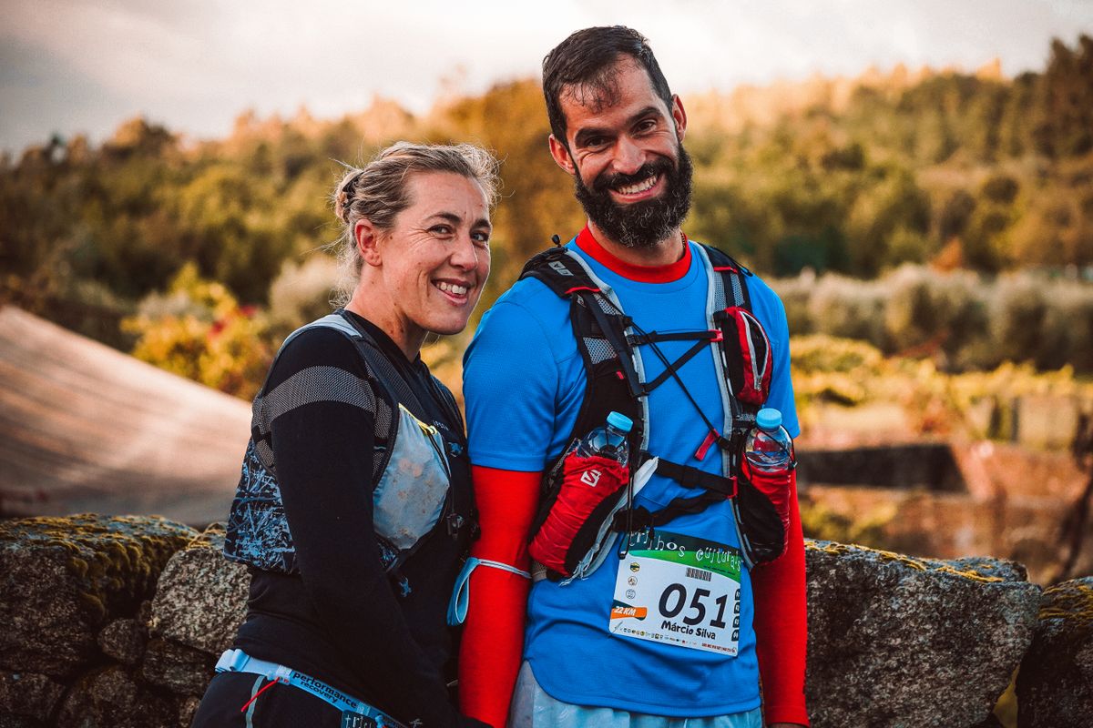Two trail participants wearing hydration vests stand together outdoors.