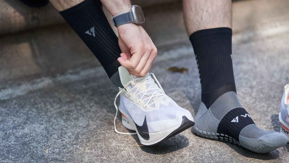 A runner tries a white running shoe while wearing sports socks.