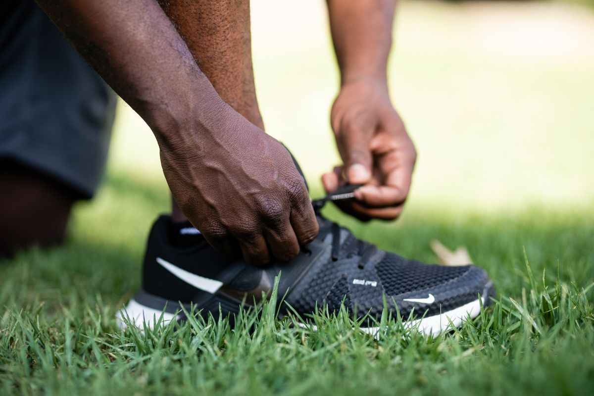 Hands tighten the laces of a black running shoe on grass.