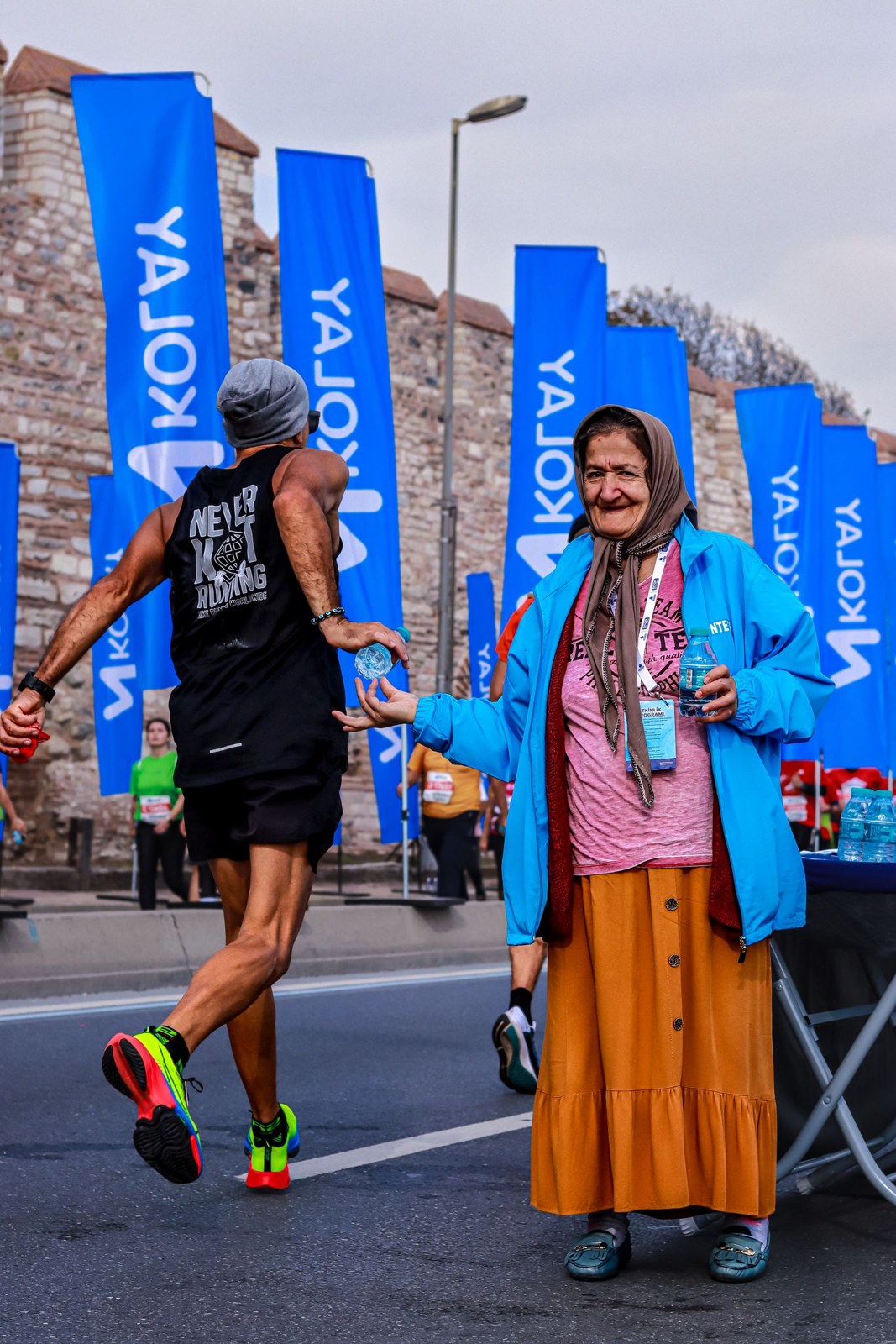 A volunteer offers water to runners at a roadside aid point.